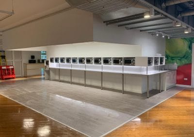 A row of microwaves is displayed on a counter in a brightly lit, modern showroom with wood and tile flooring.