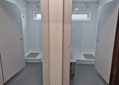 Two shower cubicles with frosted glass doors and grey floors separated by a partition in a clean, modern, and well-lit toilet facility.