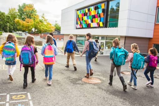 A group of children with rucksacks walk towards a modern school building with colourful panels on the exterior.